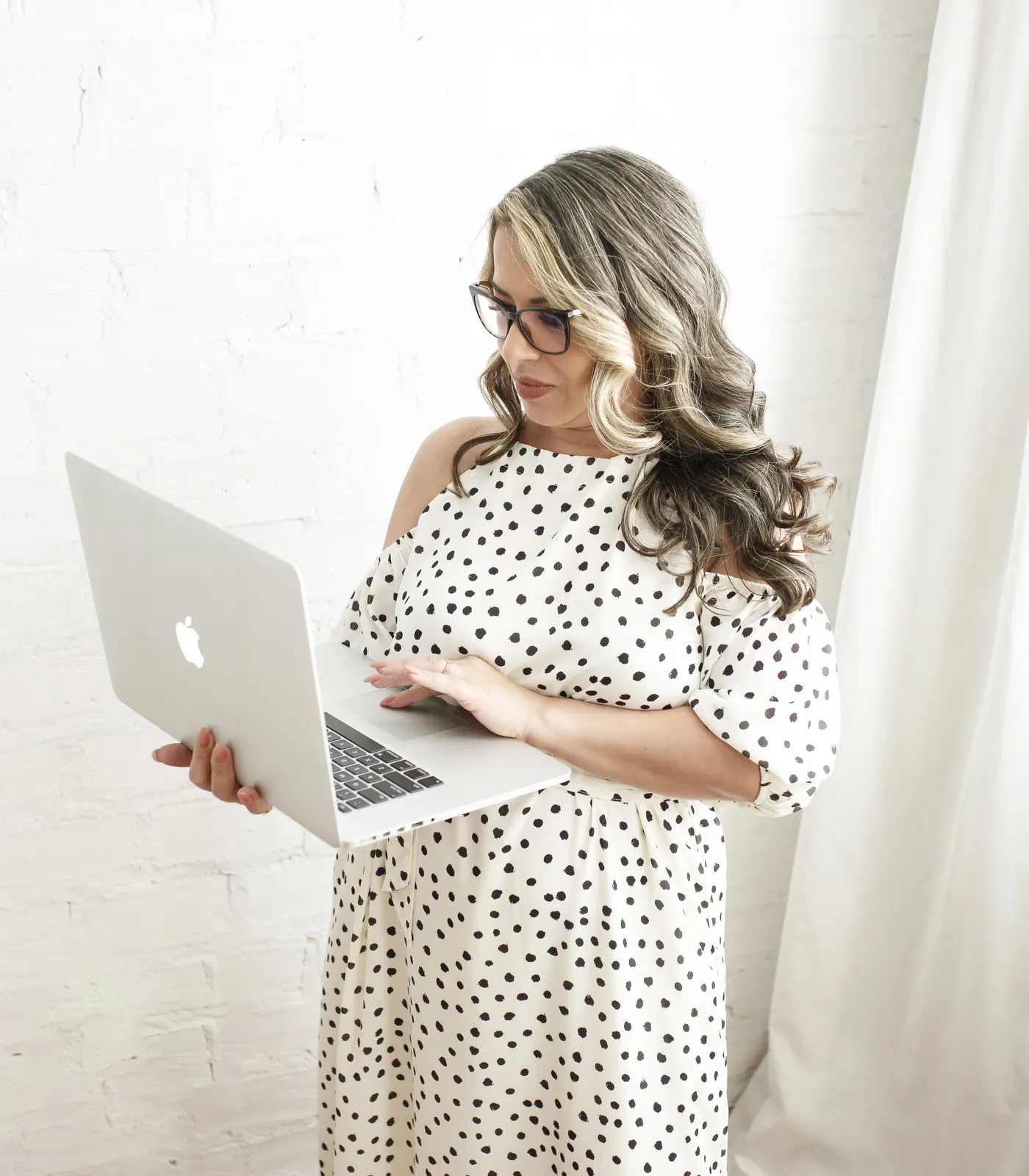 Raquel, a mulher que criou o Drop di Propósito, de pé, segurando um notebook aberto e olhando para o lado